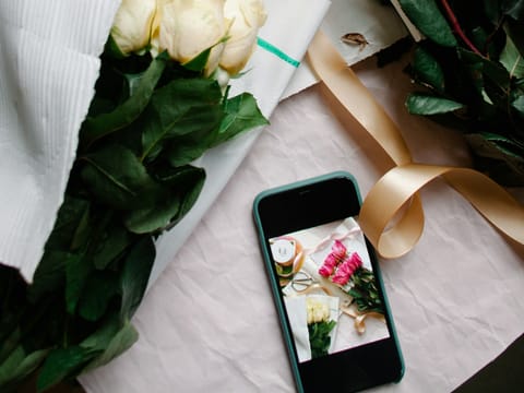 Roses and ribbon on a worktable, with a phone showing the photo just taken of the bouquet.